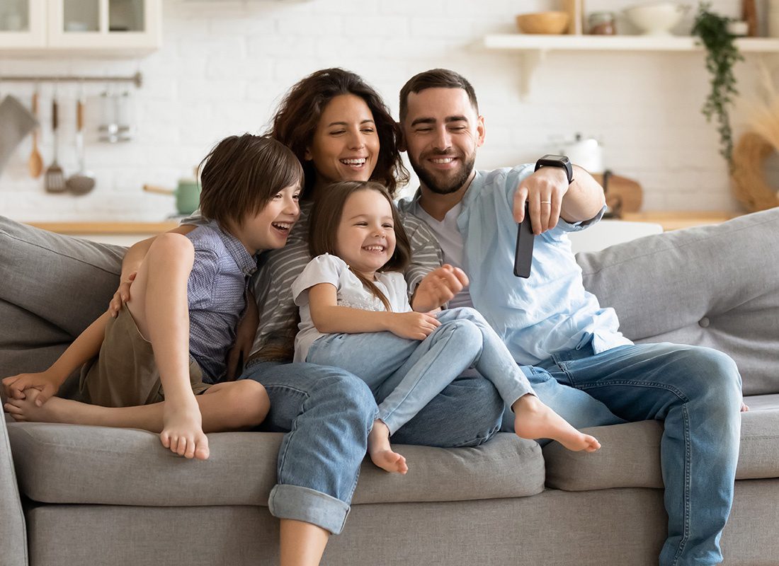 Personal Insurance - Smiling Family Sitting on a Sofa in Their Liviing Room and Looking at a Phone on a Sunny Day